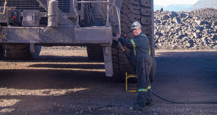 Worker in a hard hat and coveralls inspecting a large industrial truck in a mining area.